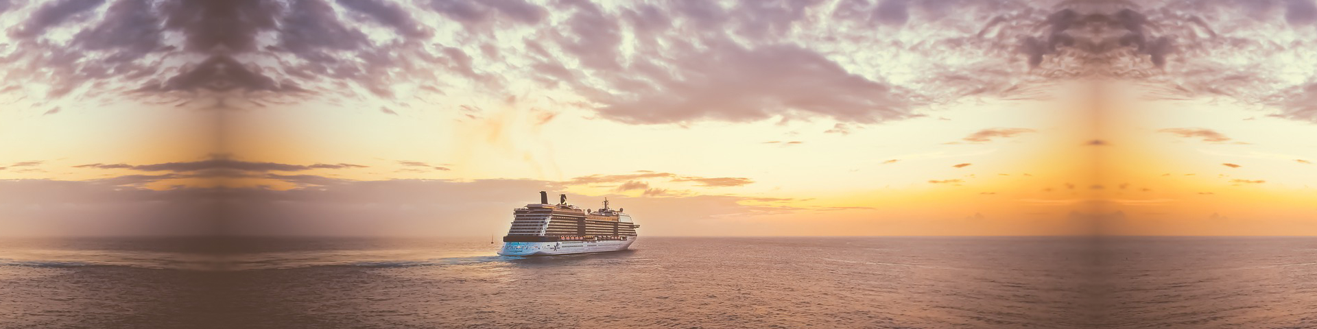 Cruise ship sailing on calm ocean waters at sunset, with vibrant colors in the sky and dramatic clouds overhead.